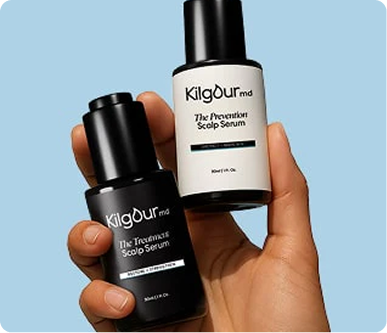 Hand holding two Kilgour MD scalp serum bottles, Treatment (black) and Prevention (white), against a light blue background
