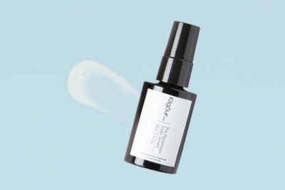 Angled view of black glass pump serum bottle showcasing clear serum smear with light blue background