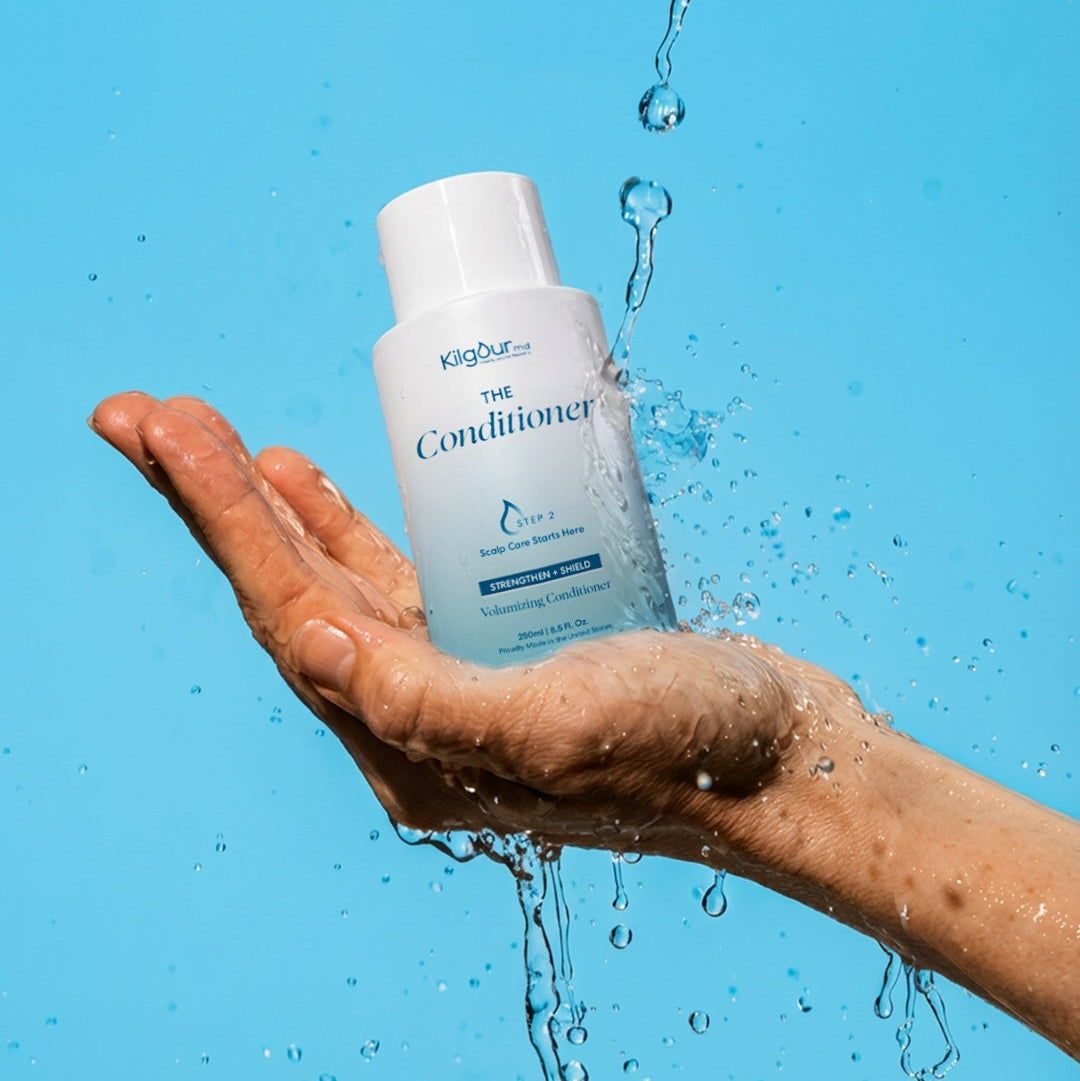 KilgourMD The Conditioner white bottle, volumizing scalp-strengthening conditioner held in a wet hand with water splashes