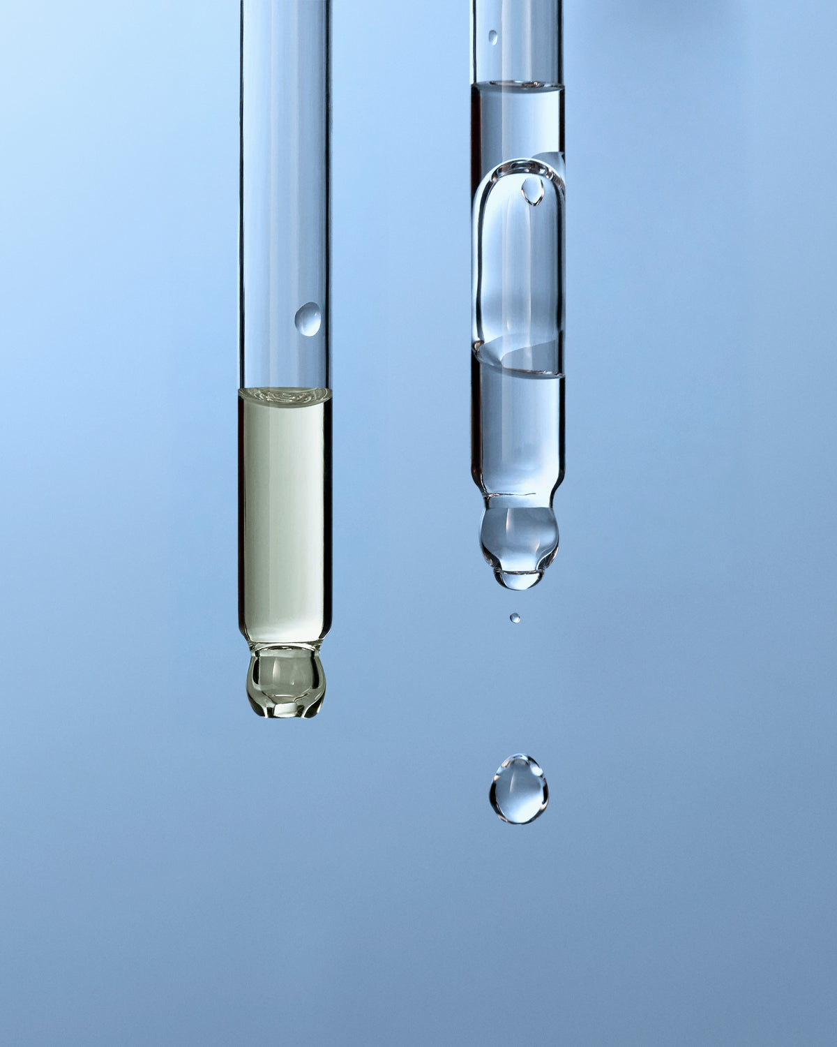 Close up of scalp serum droppers showcasing clear and pale serum with a blue background