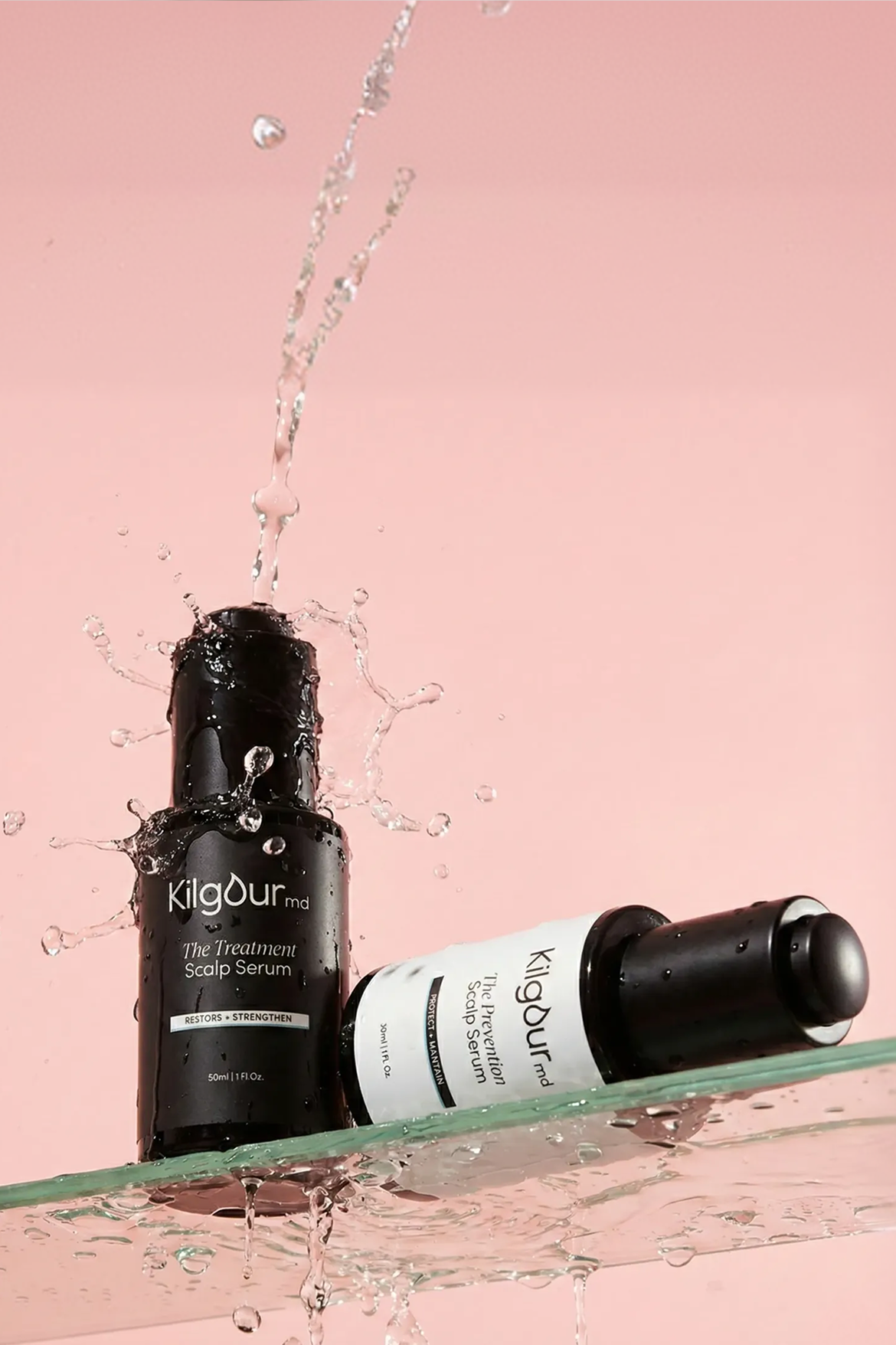 Front view of two KilgourMD scalp serum bottles with water splashing over the upright Treatment bottle on a pink background