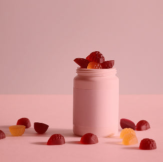 Front view of biotin gummies in a pink bottle with red and orange gummies on a pink background