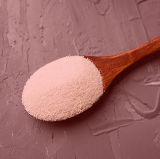 Close-up of collagen powder in a wooden spoon against a pink textured background