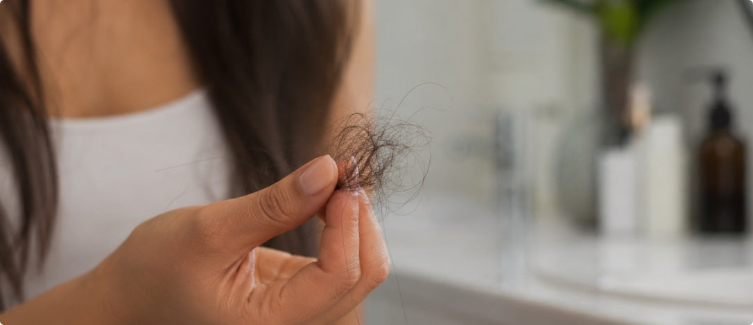 Woman examining loose hair in a bright bathroom, illustrating postpartum shedding