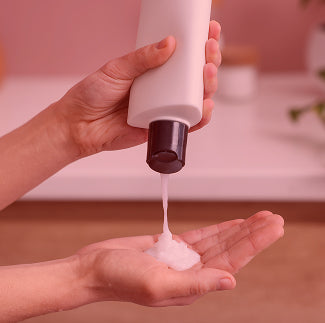 Close-up of volumizing shampoo bottle dispensing shampoo into a hand with a pink background